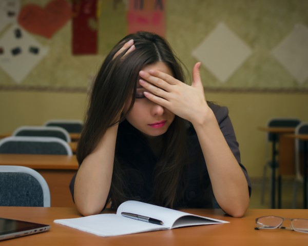 Fail the exam. Tired and bored young female student girl sits at the school desk and holds her head with her hand feel an ailment headache. Education concept.