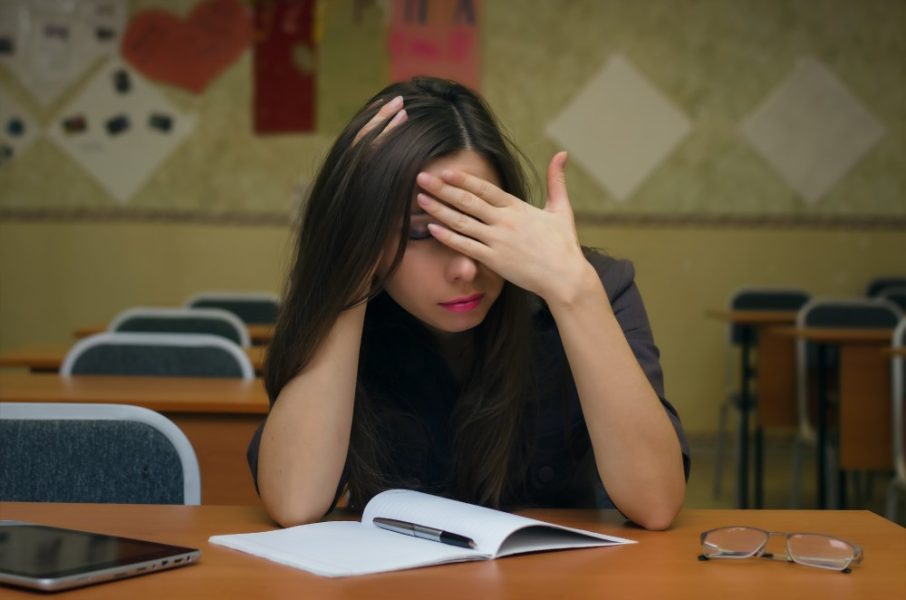 Fail the exam. Tired and bored young female student girl sits at the school desk and holds her head with her hand feel an ailment headache. Education concept.